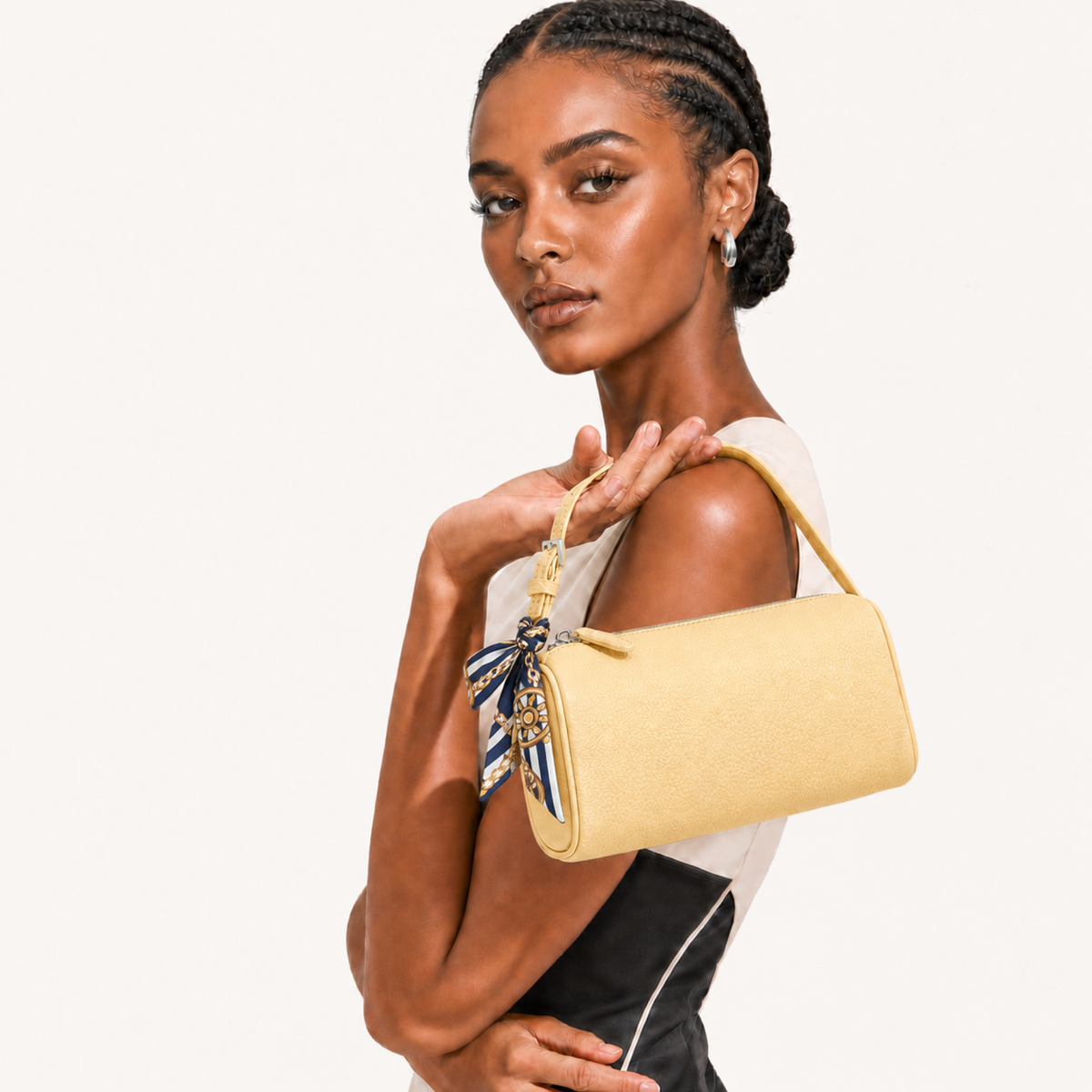 A model holds a light yellow textured leather shoulder bag with a matching top handle and a blue-and-white patterned silk scarf charm, set against a plain off-white background.