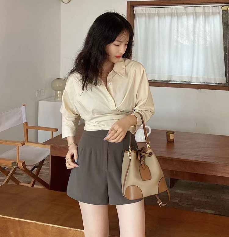 Woman holding a beige handbag in a room with wooden furniture and a window.