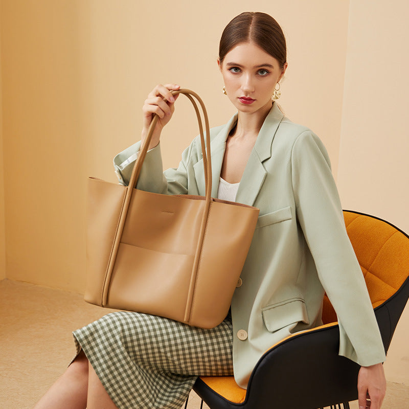 Woman holding a tan leather handbag against a beige background