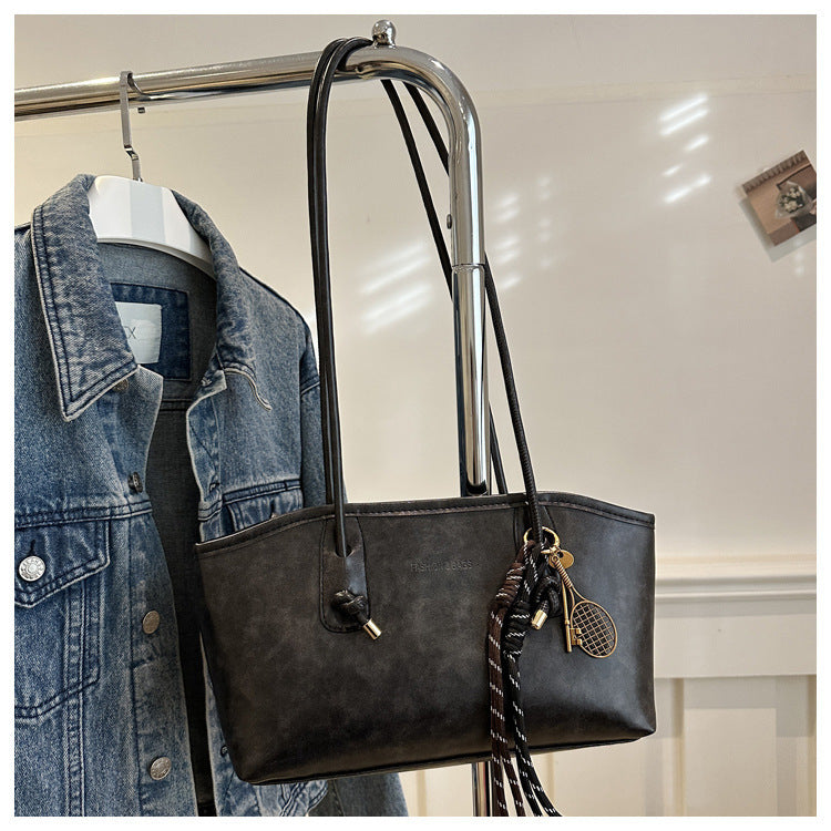 Black handbag with decorative keychain hanging on a rack next to a denim jacket.