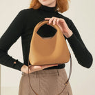 Person holding a tan handbag against a neutral background