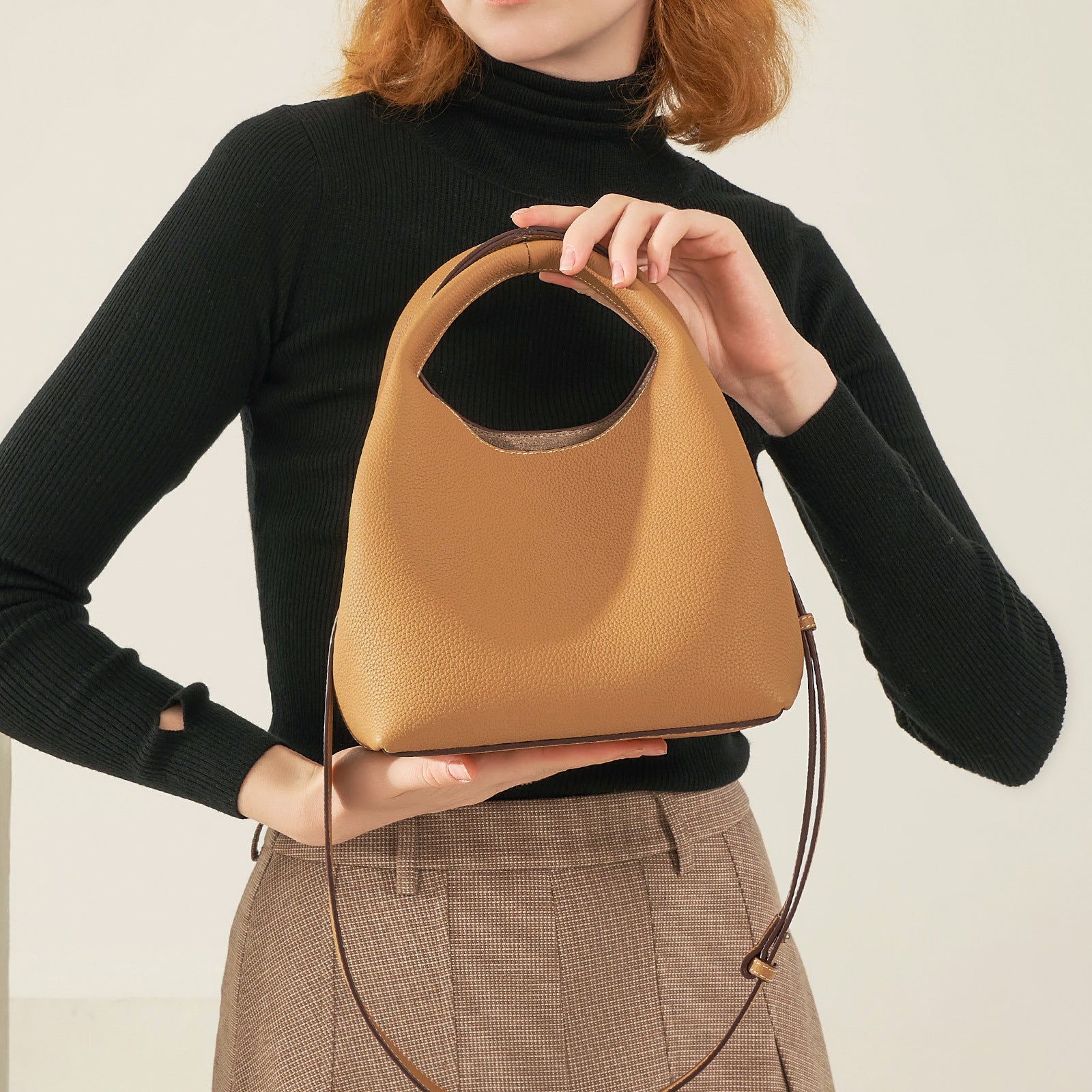 Person holding a tan handbag against a neutral background