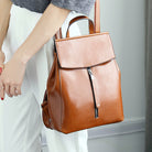 Brown leather backpack held by a person wearing white pants.
