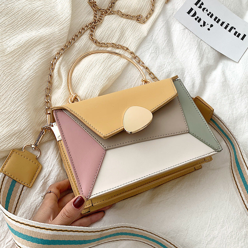 Colorful geometric handbag held by a hand on a textured fabric background