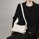 Person wearing a black outfit with a white shoulder bag on a gray background