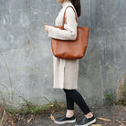 Person holding a brown tote bag against a textured wall.