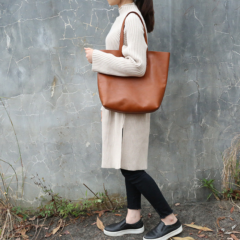 Person holding a brown tote bag against a textured wall.
