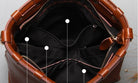 Brown leather bag with open top, showing interior and zippers.