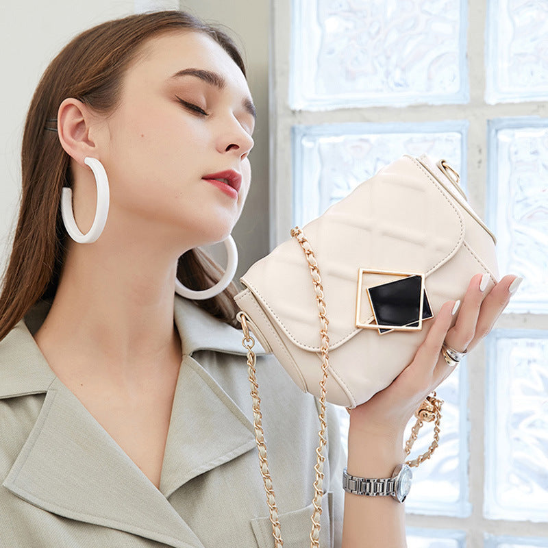 Woman holding a beige handbag with a gold chain in front of a window