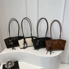 Four handbags in black, beige, and brown on a white surface with a light gray background.