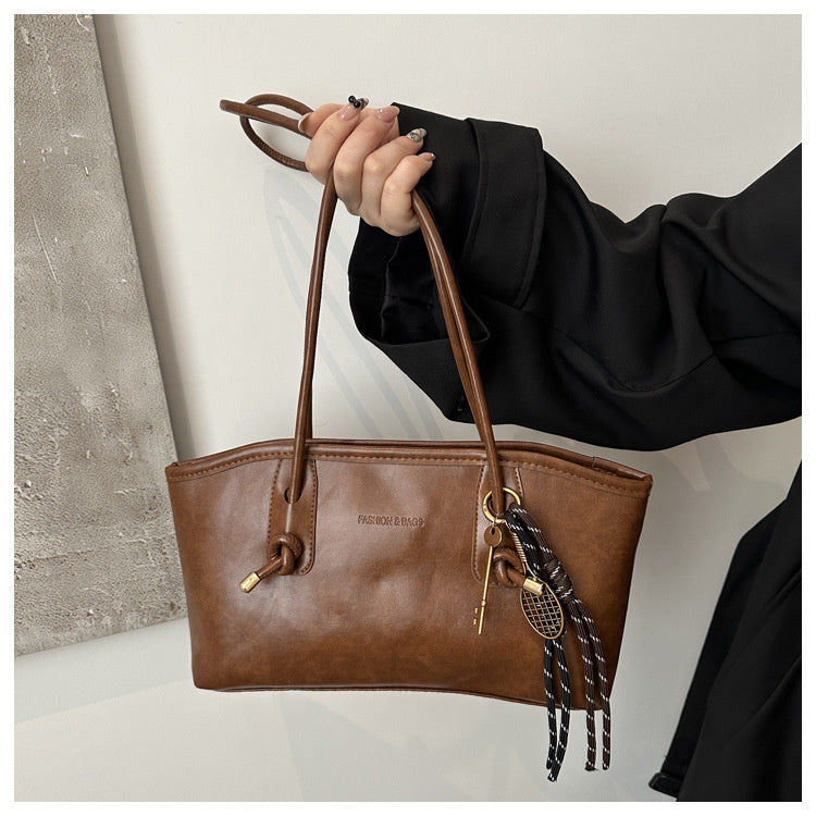 Brown leather handbag with decorative keychain held by a person wearing a black sleeve.