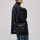 Person wearing a dark coat with a black handbag on a plain background