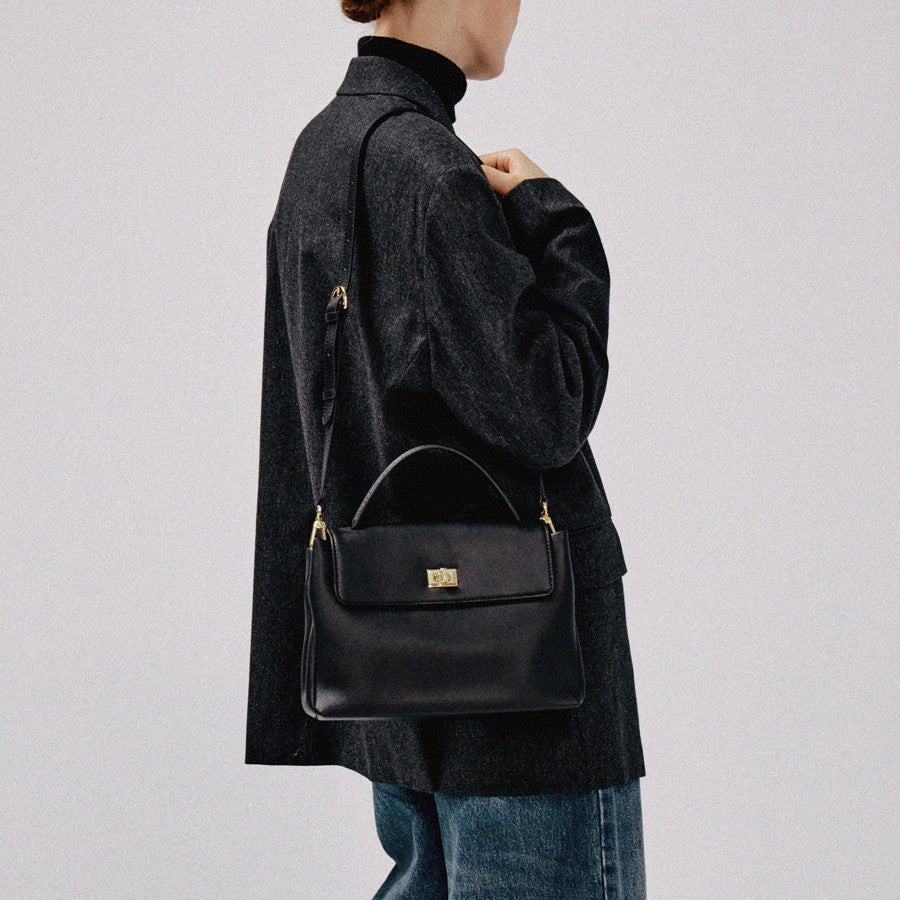 Person wearing a dark coat with a black handbag on a plain background