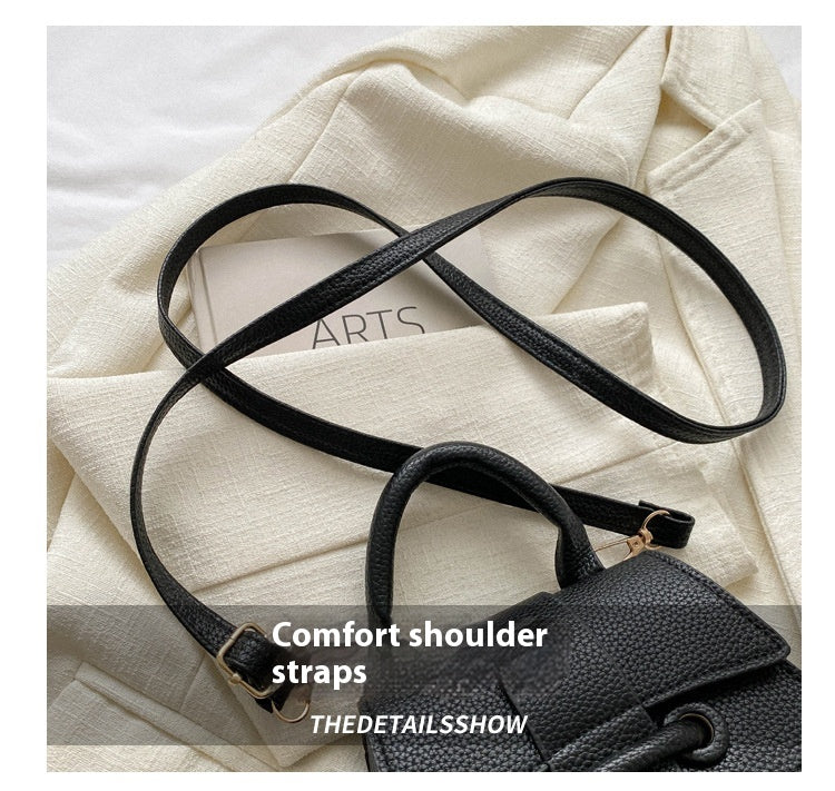 Black leather handbag with comfort shoulder strap on a white fabric background