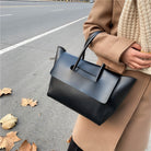 Person holding a black handbag on a street with leaves on the ground
