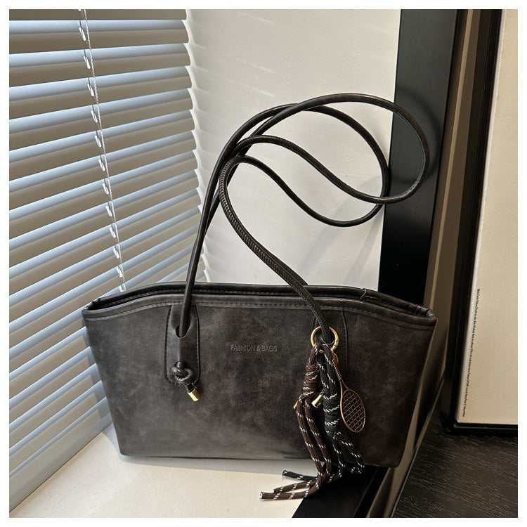 Gray handbag with a black strap and tassel on a surface with blinds in the background