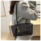 Person wearing a gray sweater with a black handbag featuring a tassel detail.