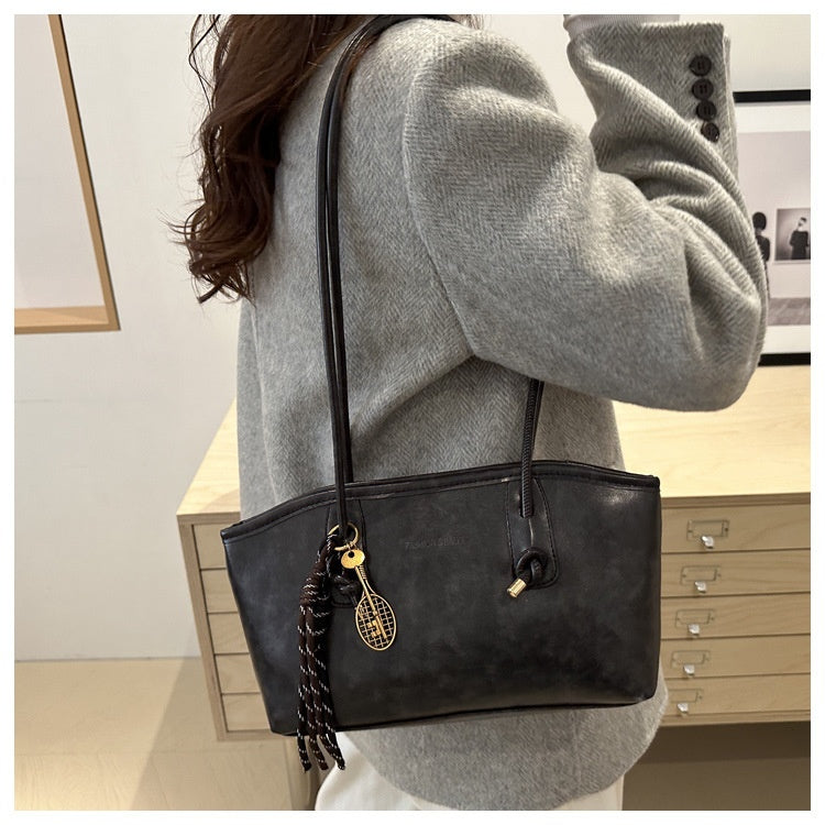 Person wearing a gray sweater with a black handbag featuring a tassel detail.