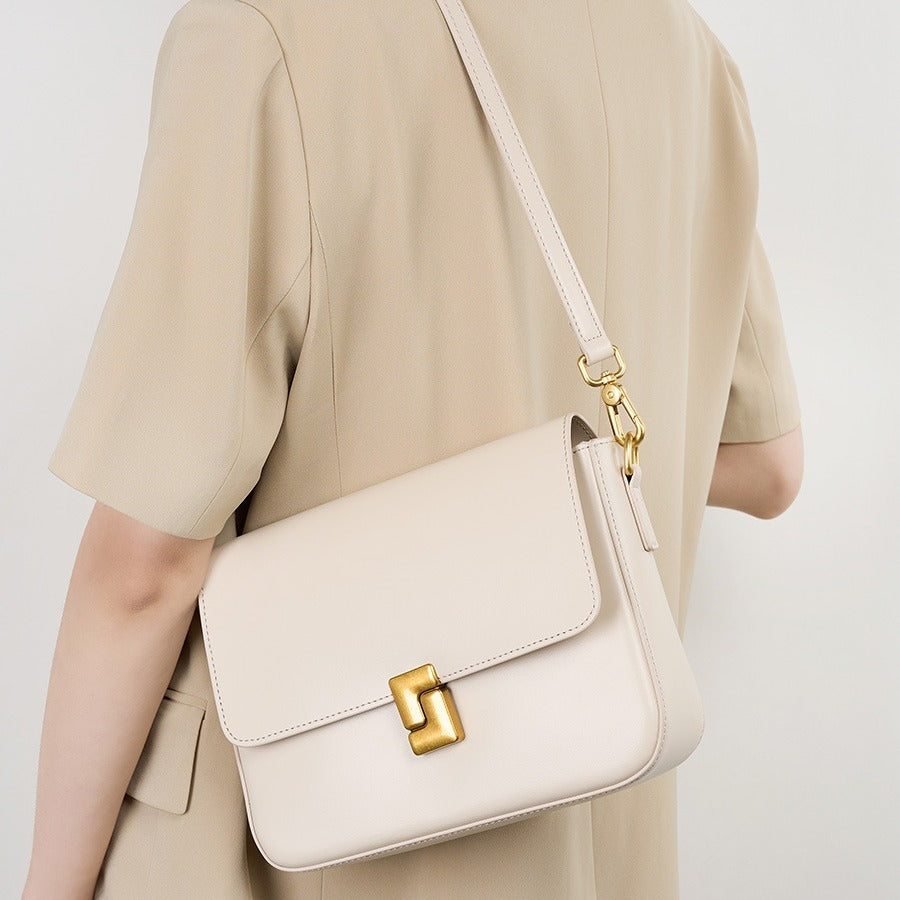 Beige handbag with gold clasp worn by a person in a beige outfit on a light background