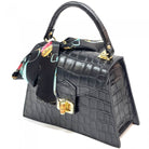Black crocodile-patterned handbag with floral detail on a white background