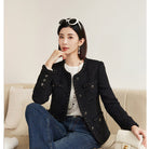 Woman sitting on a couch wearing a black jacket and blue jeans, holding a white handbag with 'NAGUAGU' branding.