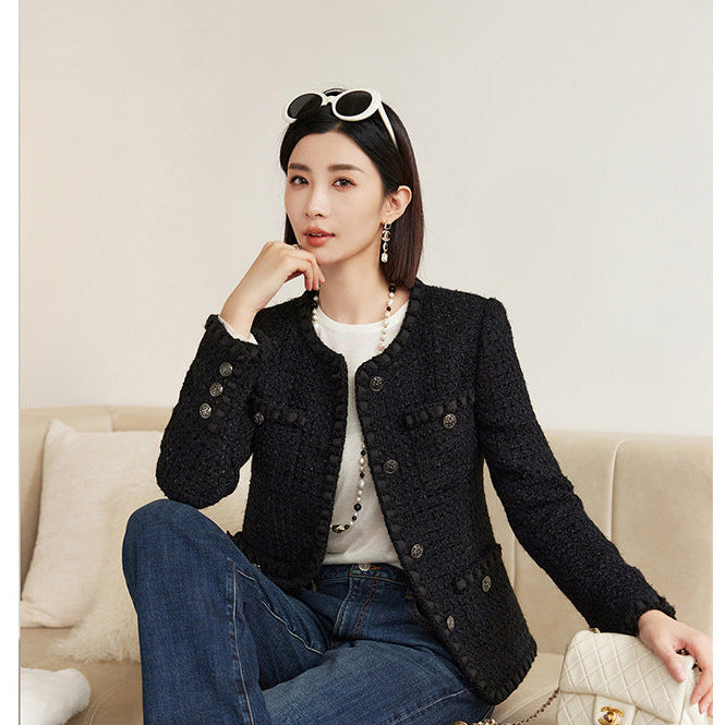 Woman sitting on a couch wearing a black jacket and blue jeans, holding a white handbag with 'NAGUAGU' branding.