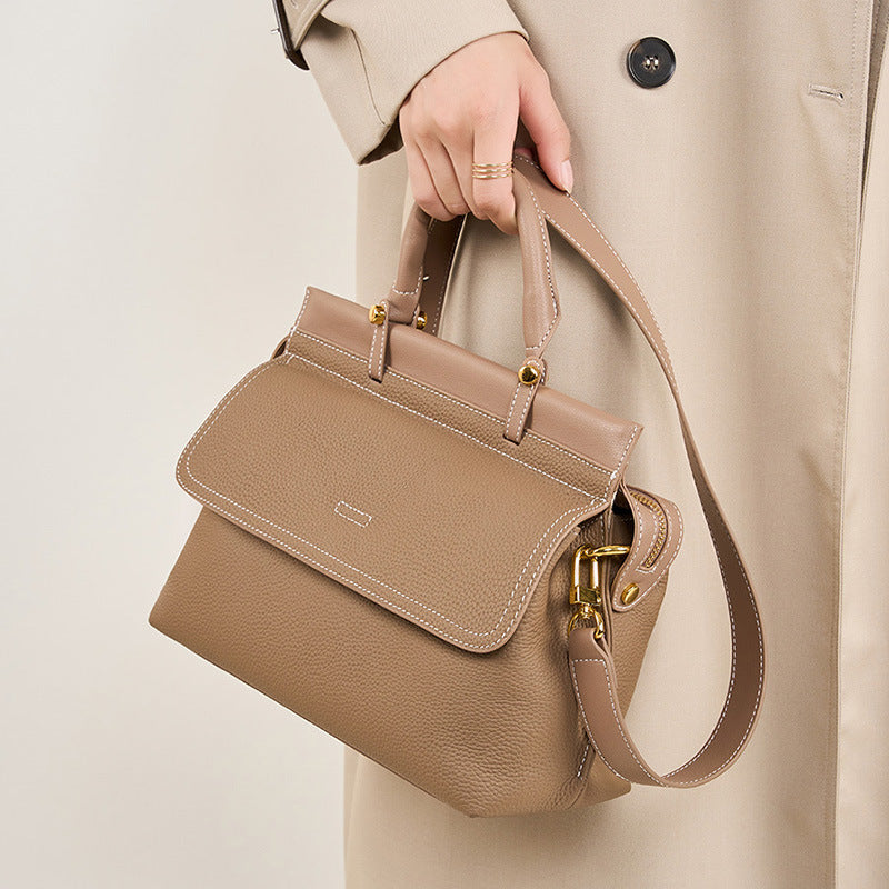Beige handbag held by a person wearing a beige coat on a light background