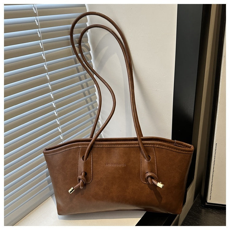 Brown leather handbag with gold accents on a surface near a window with blinds.