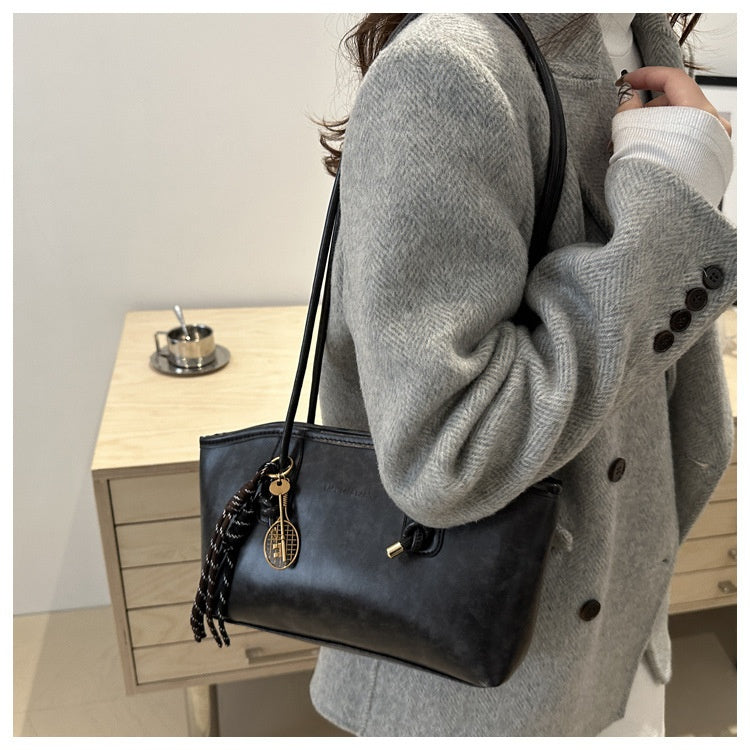 Person wearing a gray coat holding a black handbag with a braided strap.