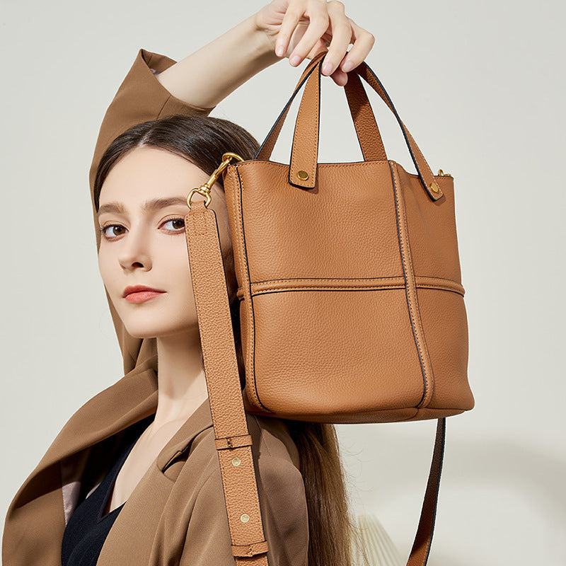 Woman holding a brown leather handbag against a neutral background