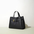Black handbag with a gold buckle on a light background