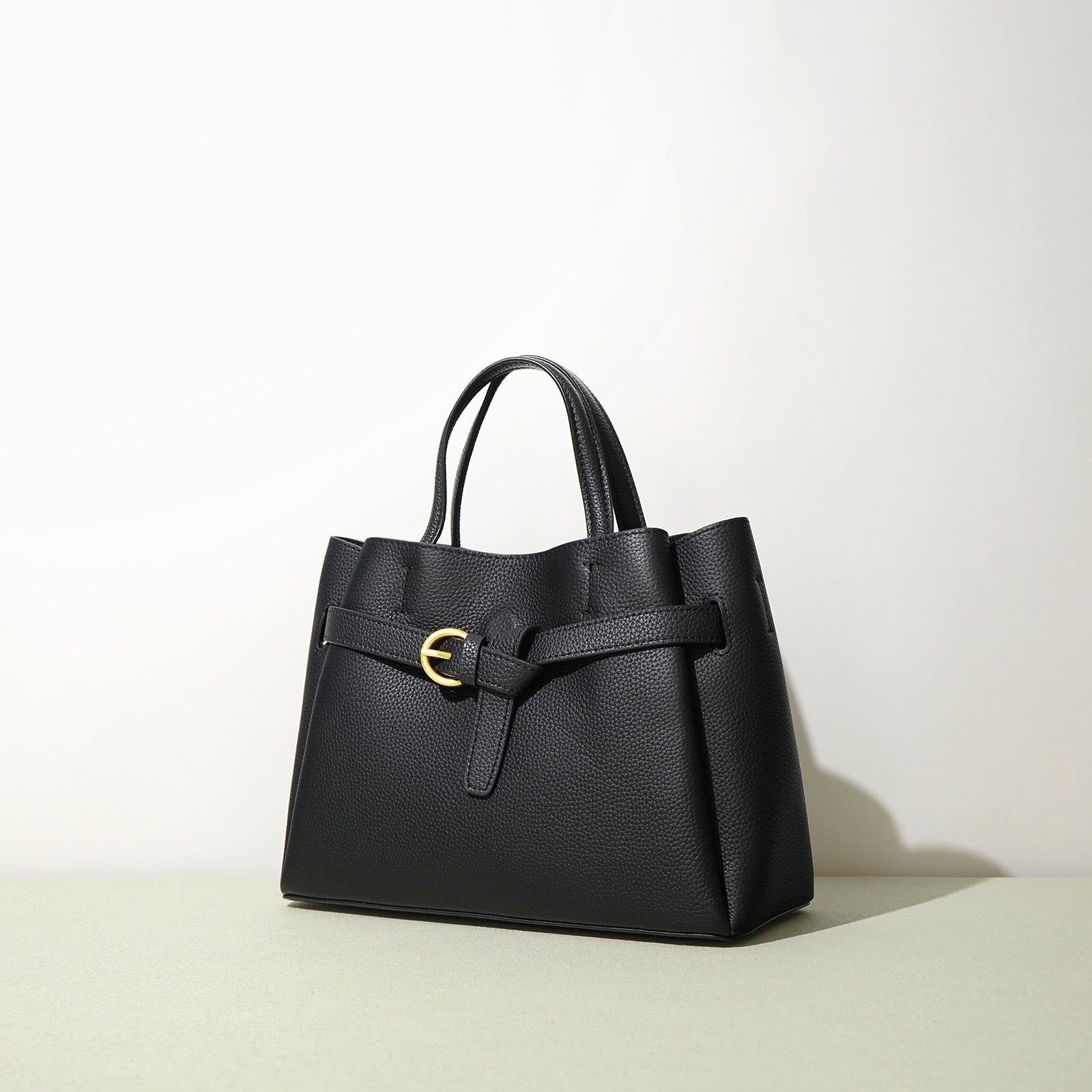 Black handbag with a gold buckle on a light background