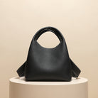 Black handbag on a beige pedestal with a beige background