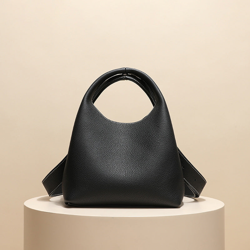 Black handbag on a beige pedestal with a beige background