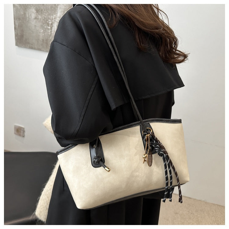 Person holding a beige handbag with black accents indoors