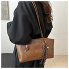 Brown leather handbag with a strap over a person's shoulder, against a neutral background.