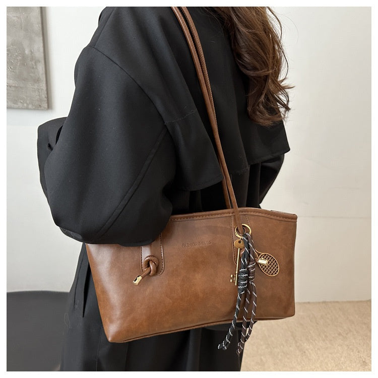 Brown leather handbag with a strap over a person's shoulder, against a neutral background.