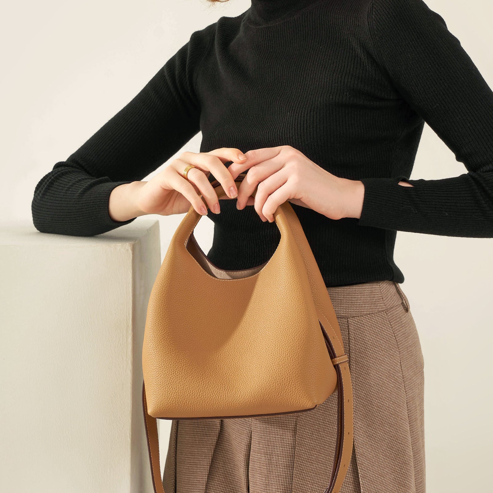 Person holding a tan handbag against a neutral background