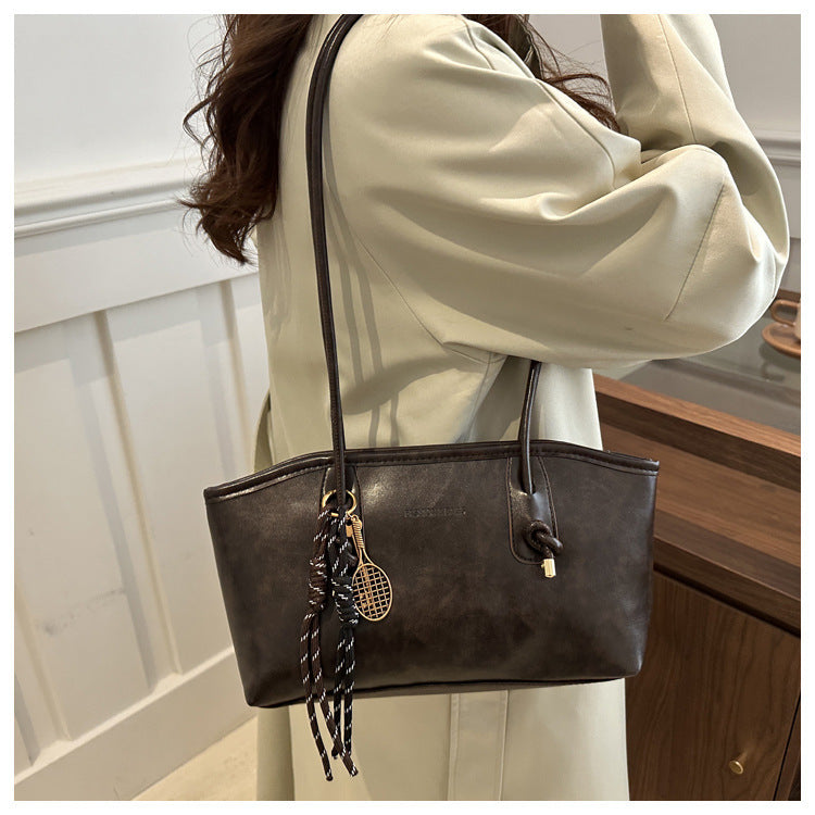 Brown leather handbag with decorative strap worn by a person indoors.