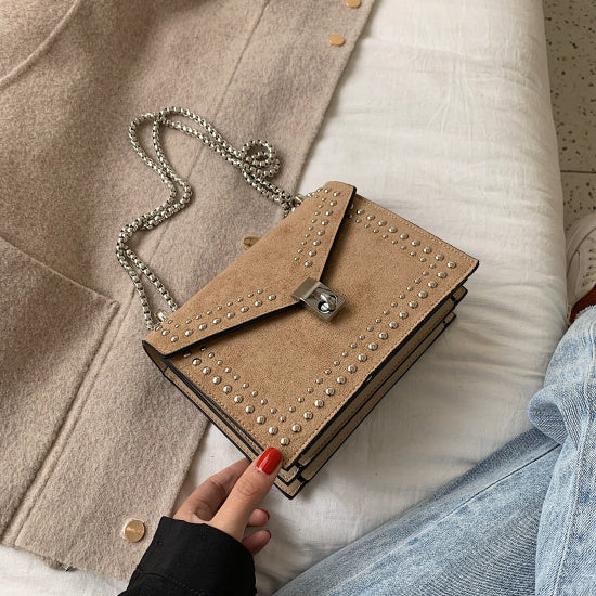 Beige handbag with studded details held by a person wearing a black jacket.
