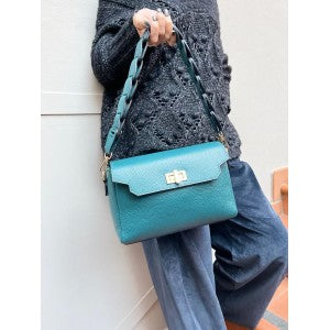 Person holding a teal handbag against a white wall