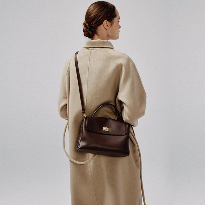 Woman wearing a beige coat with a brown leather handbag on a plain background