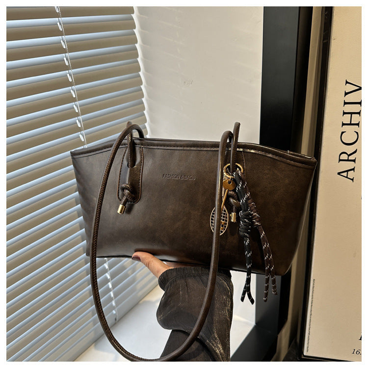 Brown handbag with decorative chain held by a hand, against a neutral background.