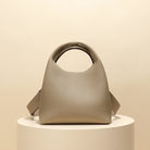 Beige handbag on a round white pedestal against a beige background