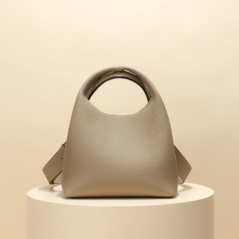 Beige handbag on a round white pedestal against a beige background