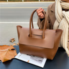 Brown leather handbag held by a person on a road with autumn leaves.