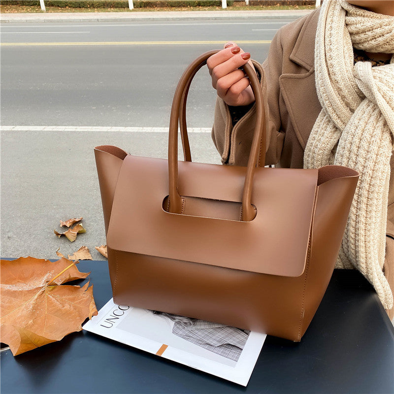 Brown leather handbag held by a person on a road with autumn leaves.