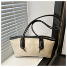 Beige handbag with black handles and trim on a surface with blinds in the background