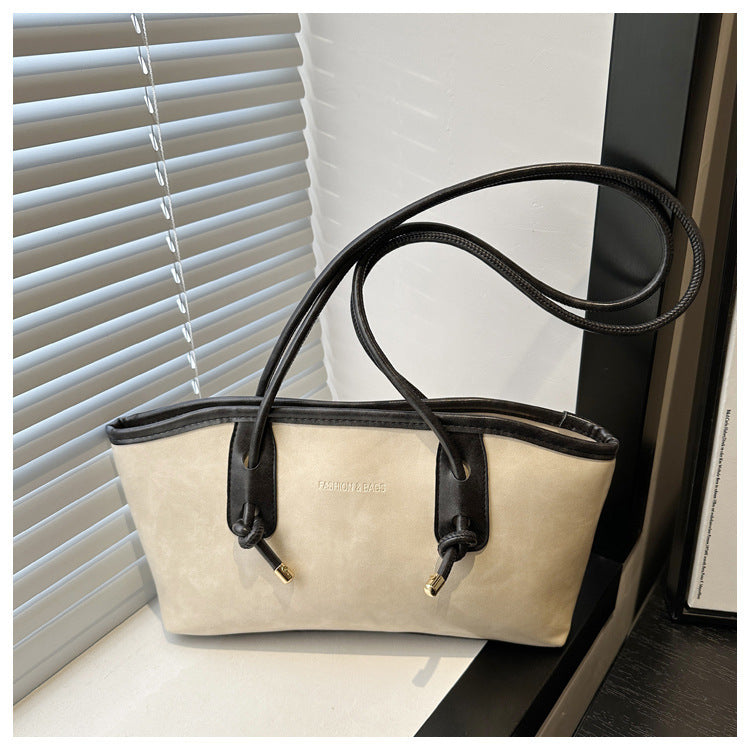 Beige handbag with black handles and trim on a surface with blinds in the background