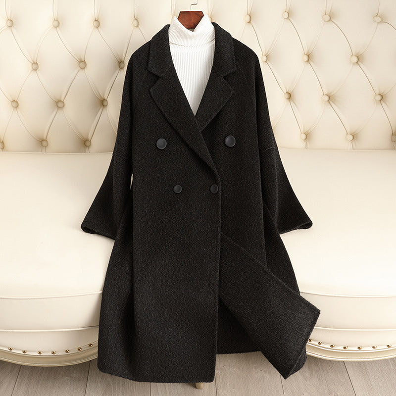 Black coat displayed on a mannequin against a decorative wall.